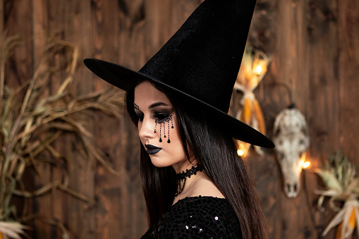 young girl in the image of a witch, wearing a black hat and a black dress with a make-up, witchcraft and hallowenn
