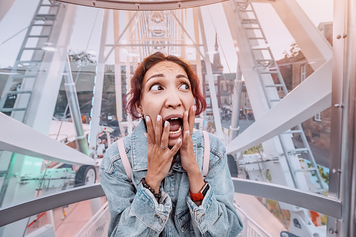 Afraid girl in the Ferris wheel is experiencing a panic attack due to fear of heights. The ride broke down and got stuck. Psychological phobias and problems