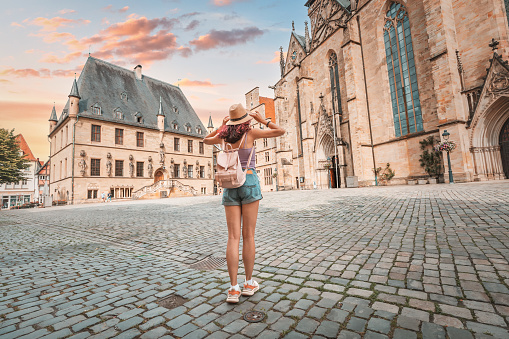 Happy woman tourist with backpack enjoying panorama of the city hall rathaus and market square of the old town of Osnabruck in Germany