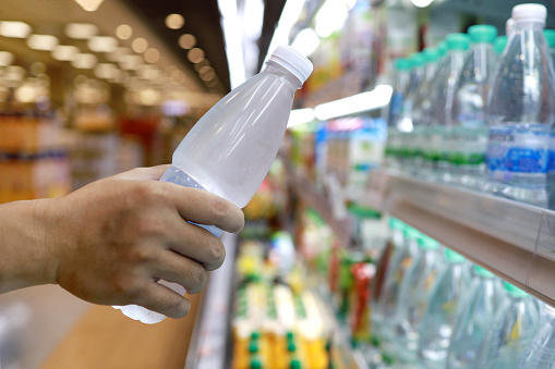 Cropped shot of a man buying a cold bottled water, taking from a open refrigerator in a grocery store