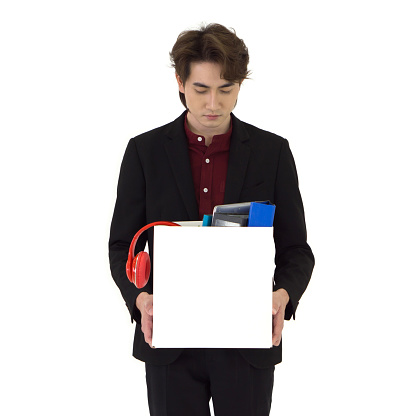 Young asian businessman in black suit feel sad, stressed and unhappy face holding paper box of belongings collected from office in the get fired day. Idea for unemployed person, work crisis.