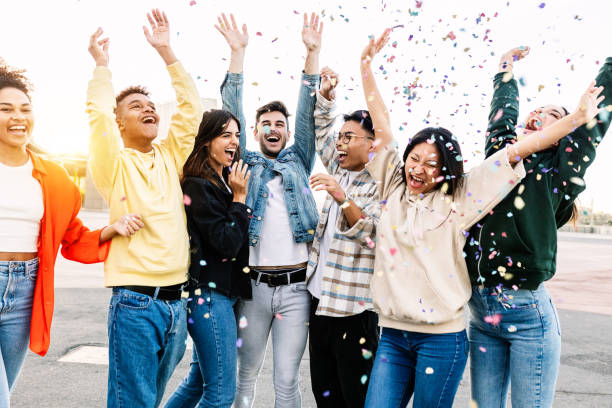 Group of diverse young friends celebrating together throwing confetti at party stock photo