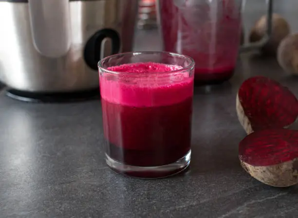Homemade beetroot juice. Served in a drinking glass on kitchen table with juicer in the background