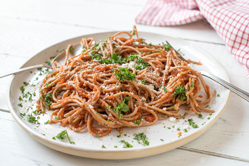 Homemade fresh cooked italian tomato sauce. Served with whole wheat spaghetti and grated parmesan cheese on a white plate isolated on white wooden table background