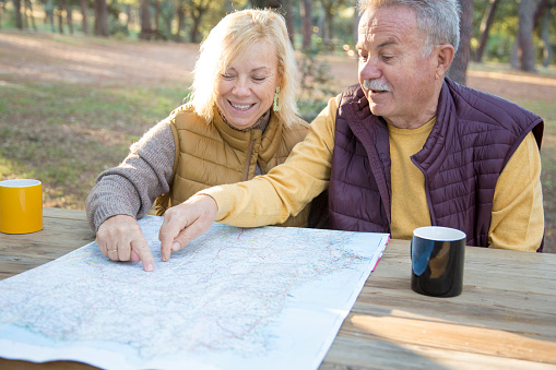 Mature couple pointing a map while drinking coffee in a picnic area in the mountain