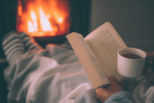 Man resting with cup of hot drink and book near fireplace