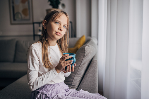 One girl, young girl sitting on sofa at home, she is holding a cup of tea.