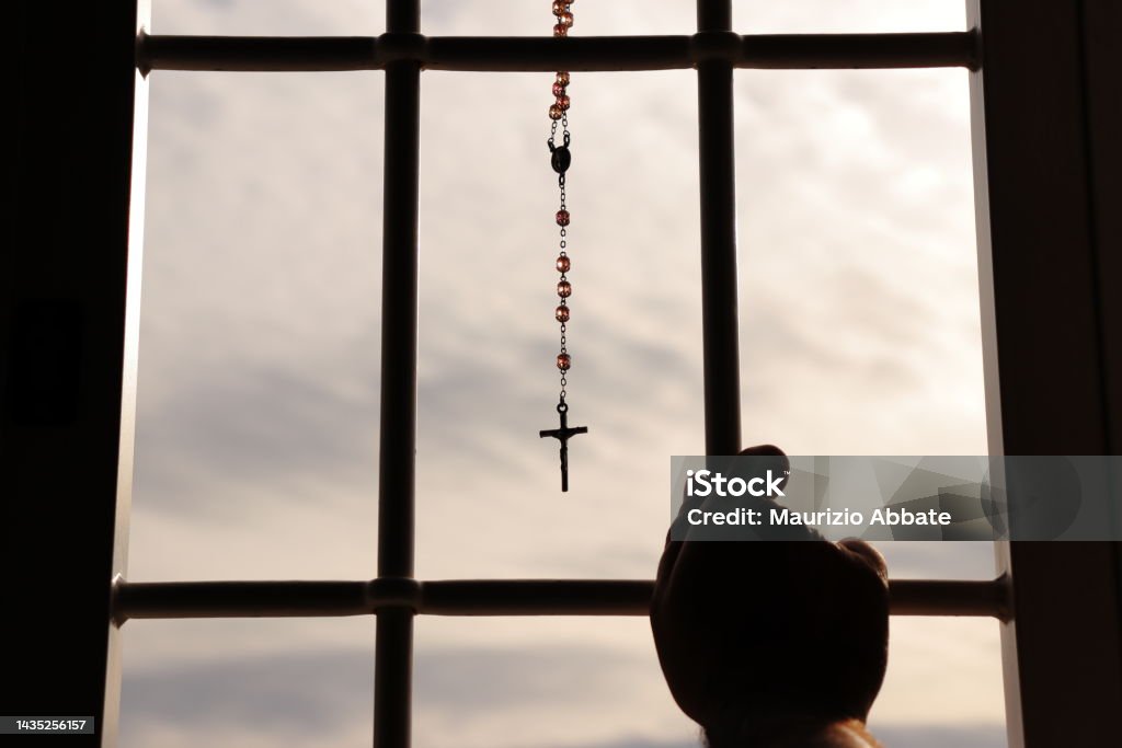 Religious rosary hanging on window with grate. Person in the act of prayer in front of the rosary hanging from a window with a grate. Prison Stock Photo