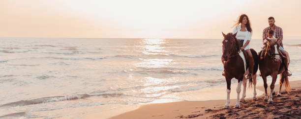 a família passa tempo com seus filhos enquanto cavalgam juntos em uma praia de areia. foco seletivo - silhouette three people beach horizon - fotografias e filmes do acervo