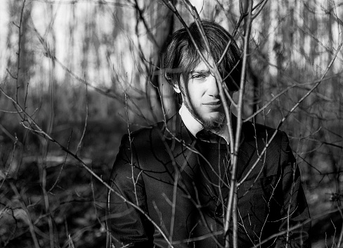 Young and elegant man portrait looking at camera while standing in the woods