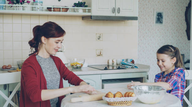 istock Young mother rolling dough and talking to little cute daughter while cooking in the kitchen on weekend. Family, food, home and people concept 1435262085