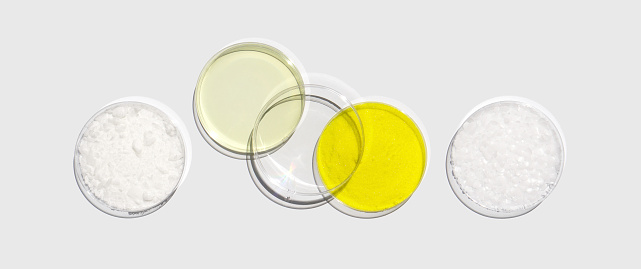 Cetyl esters wax, Poly Aluminium chloride liquid, Potassium chromate and Microcrystalline wax in Petri dish on white laboratory table. Chemical ingredient for Cosmetic and Toiletries product. Top View
