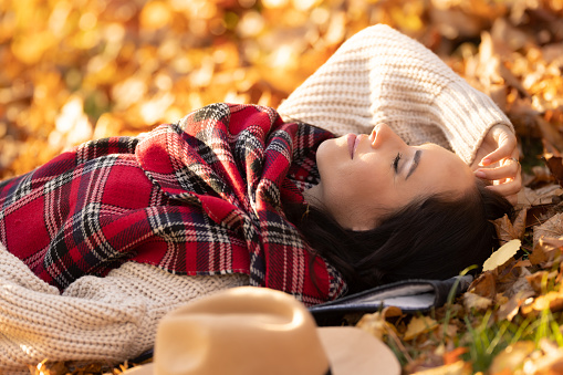 Carefree beautiful brunette lying in the park relaxing during sunny autumn sunset.