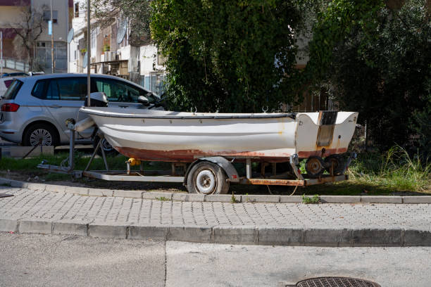 белая рыбацкая лодка, загруженная в трейлер, стоит на парковочном месте для автомобилей. старая моторная лодка в прицепе готова к транспорт - vehicle trailer nautical vessel towing yacht стоковые фото и изображения