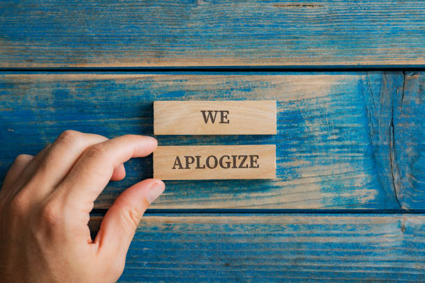 Male hand assembling a We apologize sign written on two wooden pegs stock photo