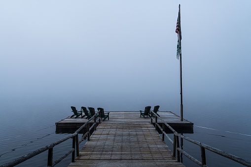A beautiful shot of a wooden dock over the lake with chairs