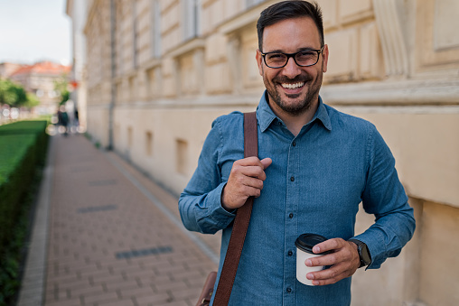 Picture of cheerful adult bearded man, getting take away coffee, posing for the picture.