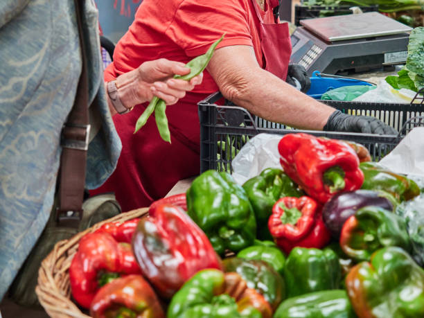 People out of focus, not recognisable in the field. Person buying fresh fruit and vegetables People out of focus, not recognisable in the field. Person buying fresh fruit and vegetables. Selective focus, basket with peppers out of focus merchants gate stock pictures, royalty-free photos & images