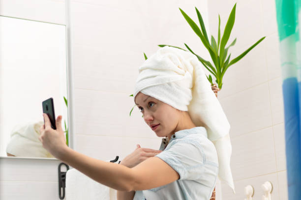 istock A young woman with a white towel on her head in a bright bathroom communicates with a smartphone with a friend in social networks. Reflection in the mirror. Selective focus 1435283651