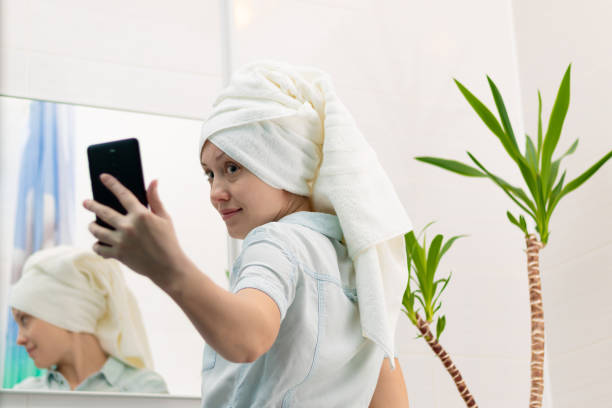 istock A young woman with a white towel on her head in a bright bathroom communicates with a smartphone with a friend in social networks. Reflection in the mirror. Selective focus 1435283662