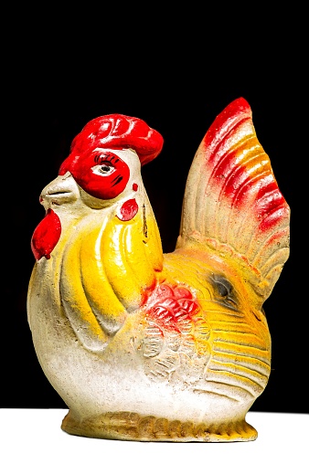A vertical closeup of a traditional Indonesian piggy bank in the shape of a chicken, black background