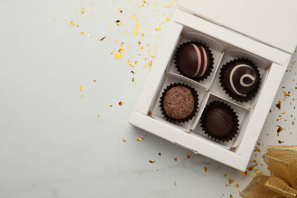 istock Different delicious chocolate truffles in box, bow and confetti on white background, flat lay. Space for text 1435284811