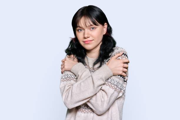 istock Young frozen woman in sweater with clasped hands gesturing coldly, on light studio background 1435285819