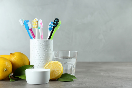 Toothbrushes, lemons and bowl of baking soda on grey table, space for text