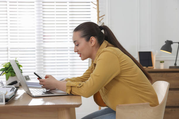 istock Young woman with poor posture using smartphone at table indoors 1435292595