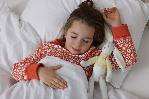 Cute little girl with toy bunny sleeping in bed, top view