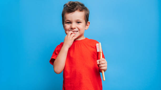 istock Smiling boy with healthy teeth brushing his teeth with a toothbrush on a blue isolated background. Oral hygiene. 1435295523
