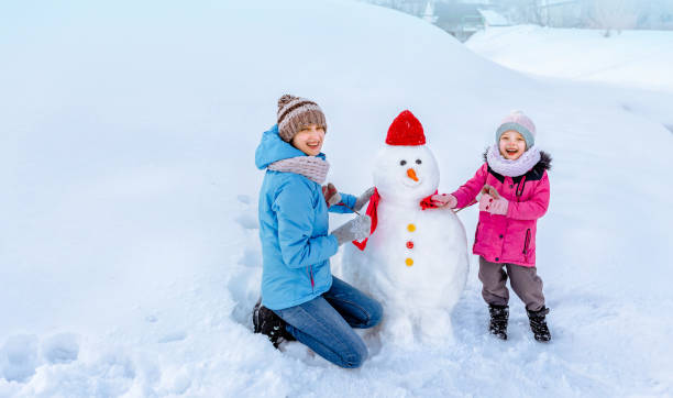 istock mom and daughter make a snowman and decorate it 1435297841