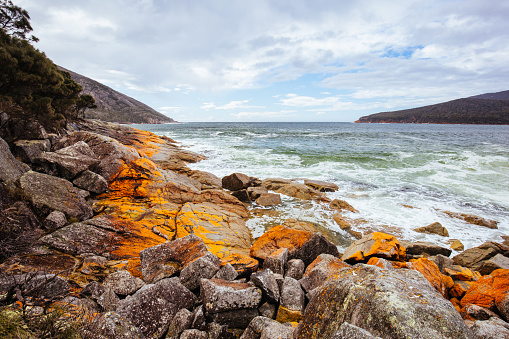 Wineglass Bay Beach and its orange lichen rocks on a rough day in the Freycinet Peninsula in Tasmania, Australia