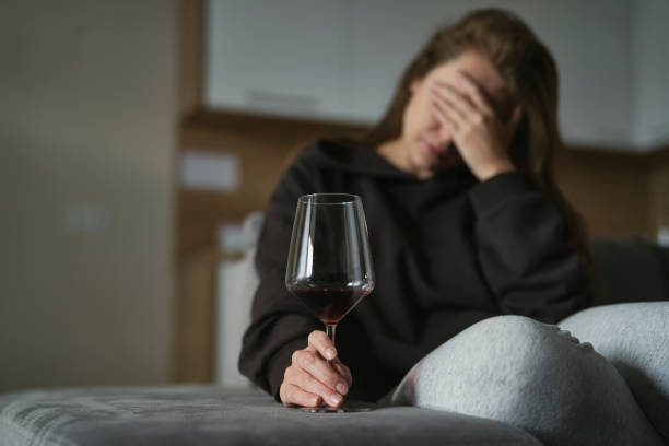 Caucasian woman with alcoholism sitting at the sofa and holding glass of wine stock photo