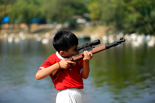 Elementary student of Indian ethnicity portrait with toy gun near lake during summer season.