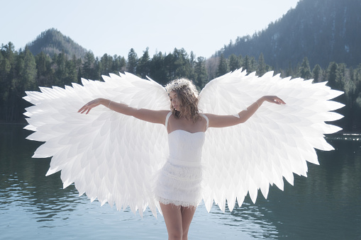 Girl dressed as an angel on the background of a forest lake
