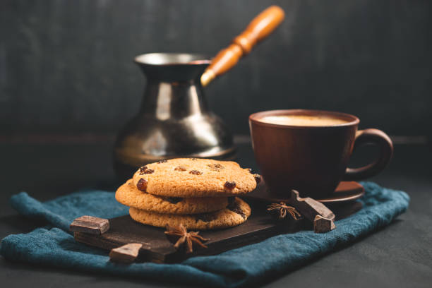 istock Crispy oatmeal cookies with raisins, coffee cup and turkish coffee pot, chocolate chunks on a dark background 1435309910