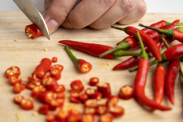 woman's hand is using a knife to cut red chili peppers for cooking