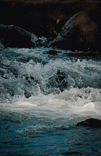 Dark blue and frothing water surrounded by rocks in turbulent river.