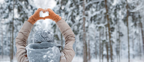 woman mittens dressed fashionable gray stands with her back makes heart gesture with her hands against background snowy winter forest happy woman walking outside woods snowy winter day. woman mittens dressed fashionable gray stands with her back makes heart gesture with her hands against background snowy winter forest irish travellers photos stock pictures, royalty-free photos & images