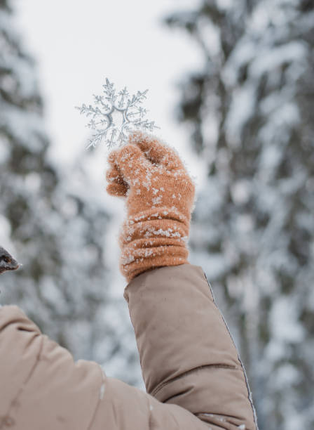 hand in mitten holding decorative transparent snowflake, winter forest natural background.
