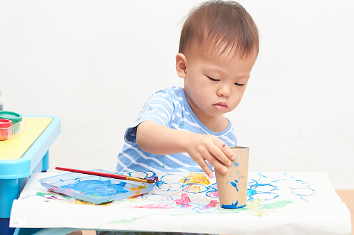 Cute little Asian 18 months, 1 year old toddler boy child painting with toilet paper roll at home, Creative Art activities for Physical Development, children's large and small muscle development