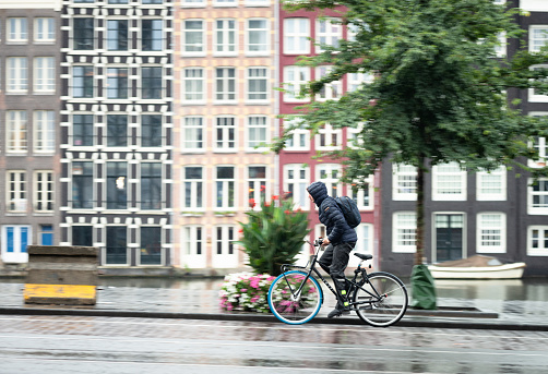 Amsterdam, Netherlands - A panning image, with the background blurred with motion, of a cyclist commuting during heavy rainfall in the city.