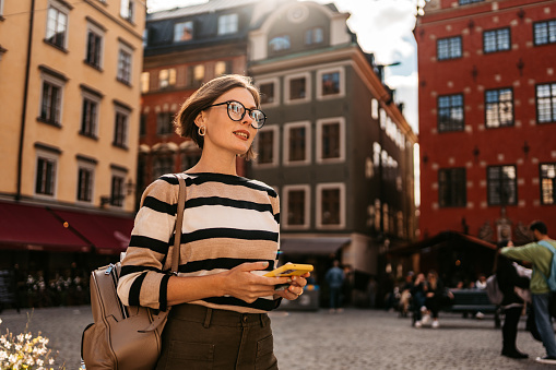 Beautiful young woman using phone outdoors on the street in Stockholm, Sweden on a sunny day.