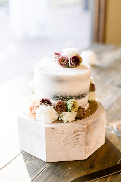 istock Elegant little wedding cake with white icing and roses (maroon, white, fall colors) on a rustic table. 1435328506