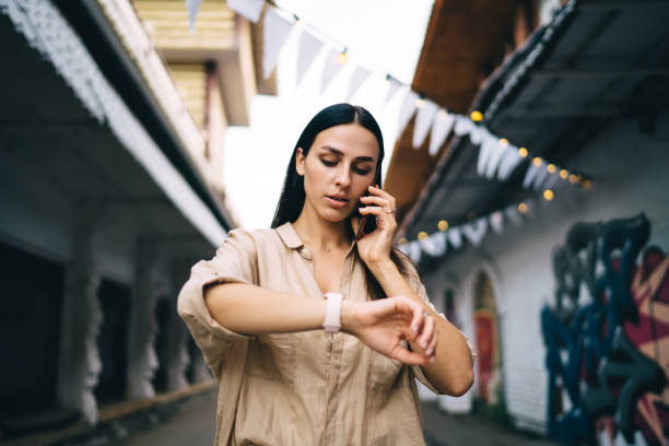 istock Serious young lady talking on smartphone while checking time on wristwatch on street 1435336348