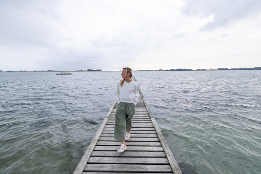 One female on wooden lake pier relaxing and enjoying sea view scenery, travel in Northern Europe concept