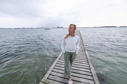 One female on wooden lake pier relaxing and enjoying sea view scenery, travel in Northern Europe concept