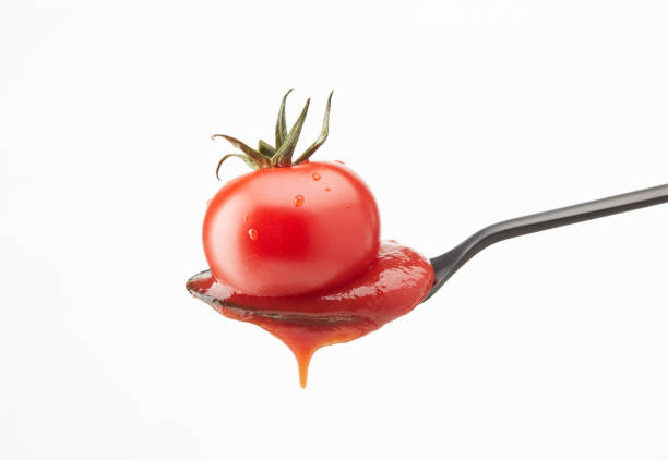 Red tomato and ketchup pouring out of a spoon on a white background. Shallow depth of field