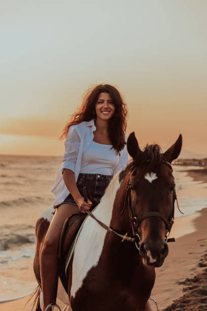 kobieta w letnich ubraniach lubi jeździć konno po pięknej piaszczystej plaży o zachodzie słońca. selektywne ustawianie ostrości - cowboy horseback riding nature blue zdjęcia i obrazy z banku zdjęć